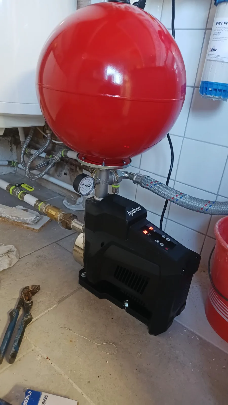 Grupo de presión con depósito rojo y manómetro instalado en un cuarto de servicio