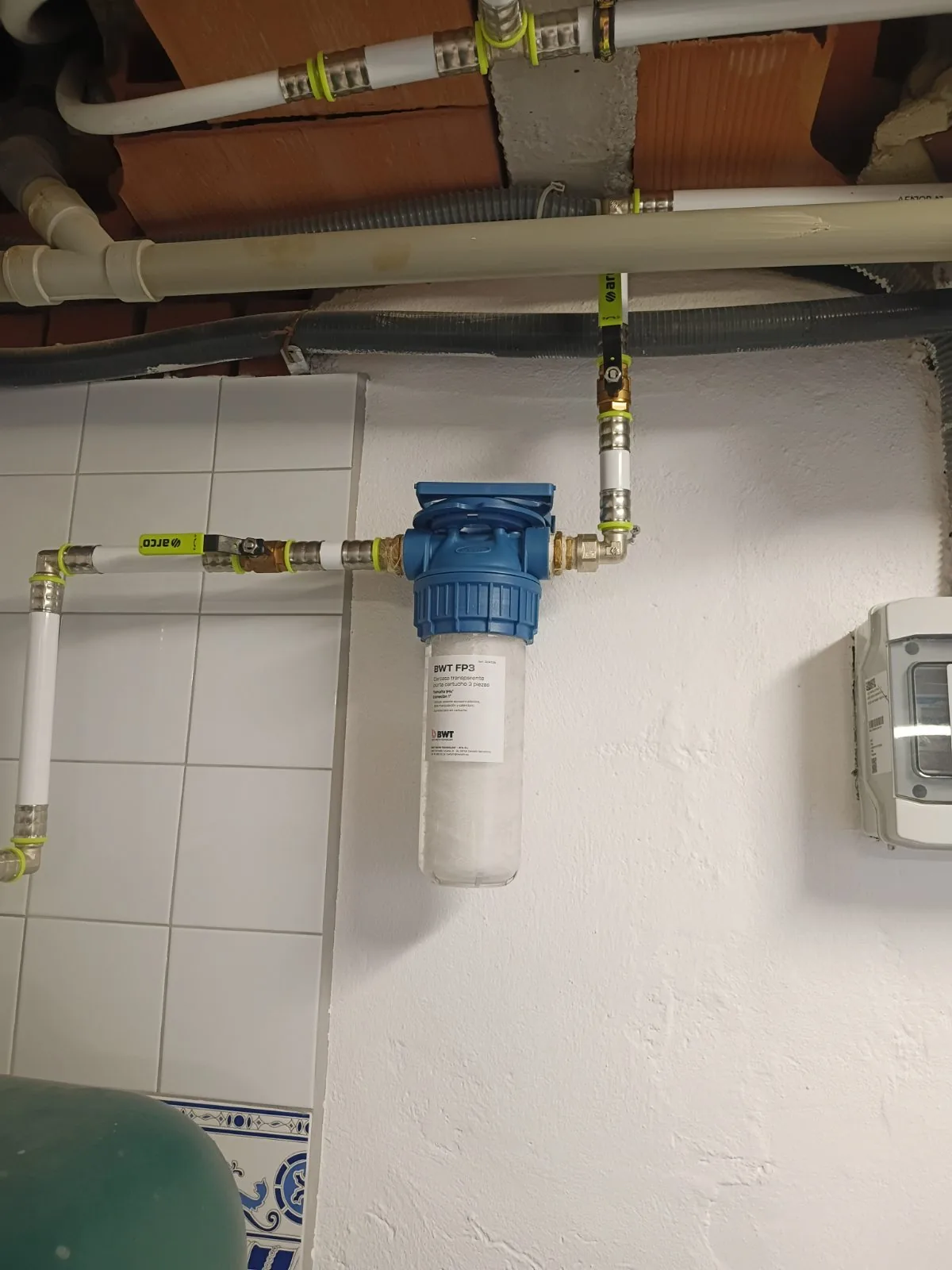 Filtro de agua azul instalado en la pared con tuberías multicapa y llaves de paso