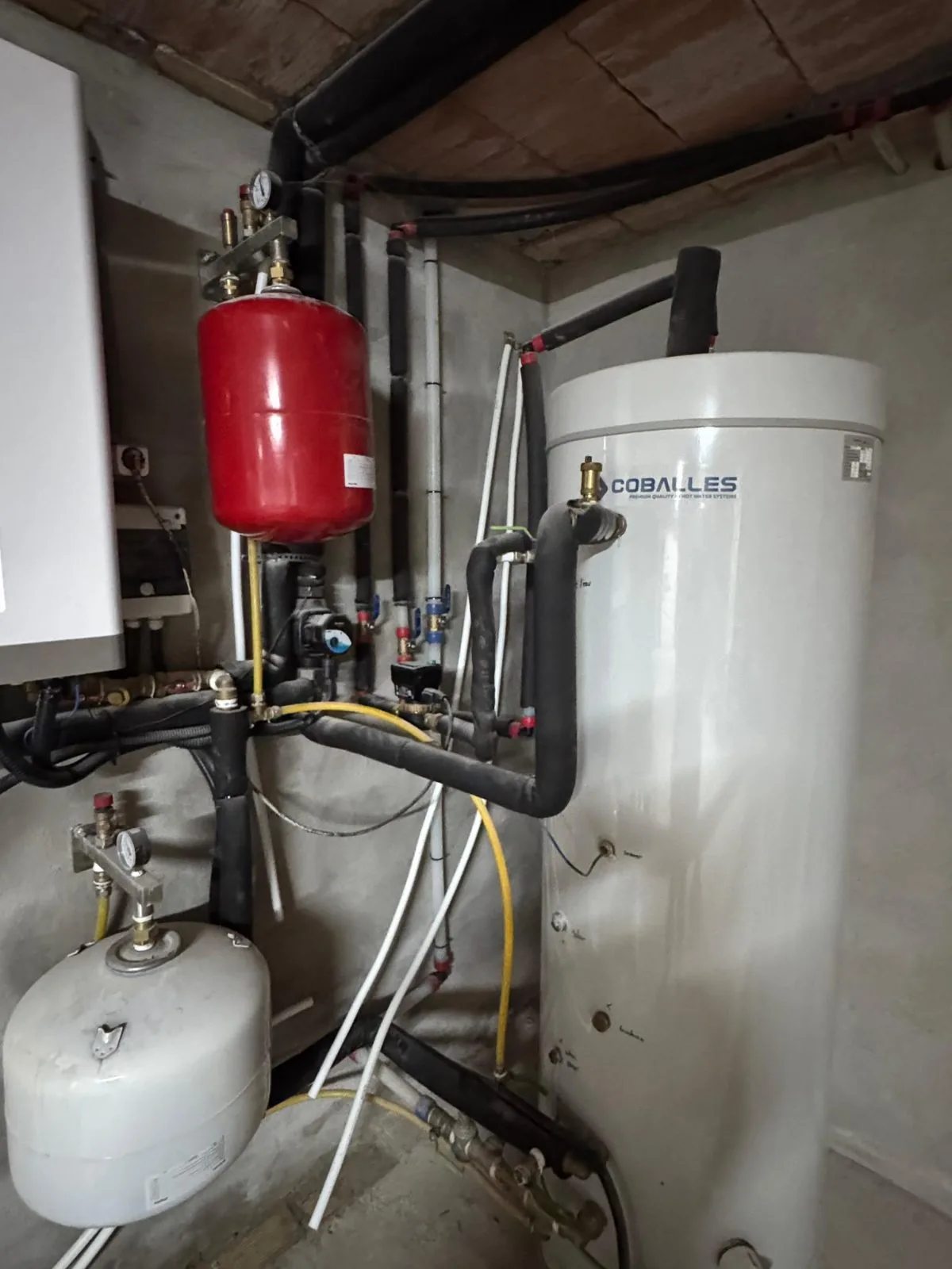 Sala técnica con acumulador de agua, vasos de expansión rojo y blanco y tuberías aisladas